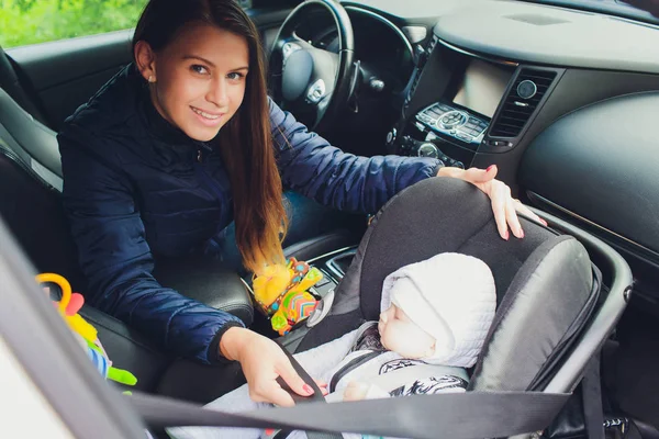 Femme attachant son fils sur un siège bébé dans une voiture . — Photo