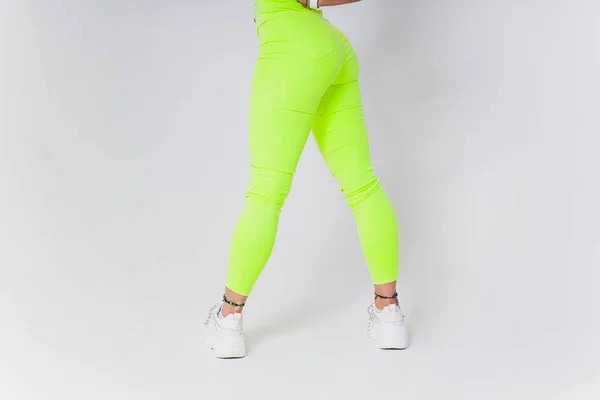 Poten in groene legging en witte sneakers zijn op een witte tegel. Rond het object is een grijze achtergrond. Het concept van sportschoenen en comfort. — Stockfoto