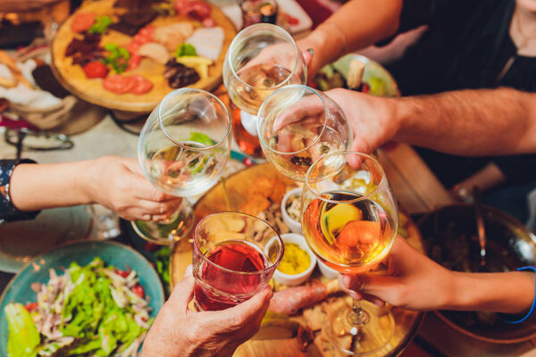 Close up shot of group of people clinking glasses with wine or champagne in front of bokeh background. older people hands