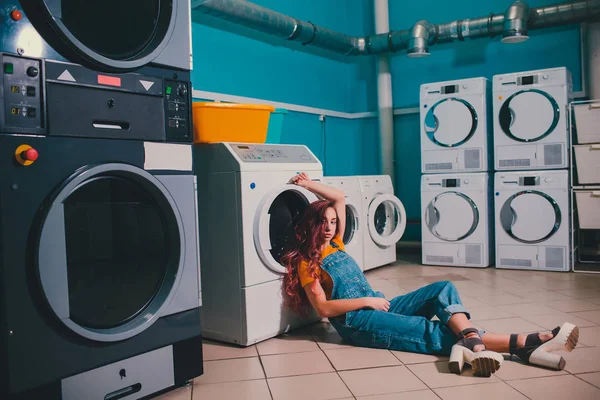 Wanita muda yang mencari pakaian di mesin cuci drum di binatu . — Stok Foto