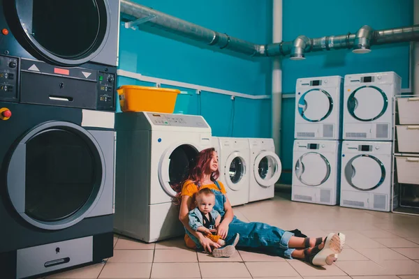 Молодая женщина ищет одежду в барабане стиральной машины в прачечной . — стоковое фото