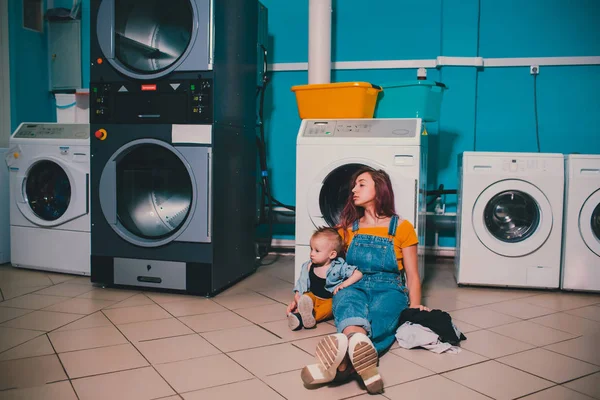 Wanita muda yang mencari pakaian di mesin cuci drum di binatu . — Stok Foto