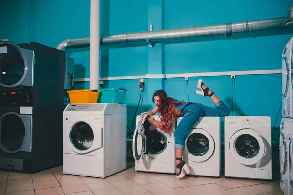 Wanita muda yang mencari pakaian di mesin cuci drum di binatu . — Stok Foto