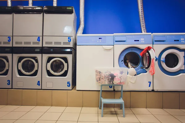 Professionelle Waschmaschinen mit Körben voller Kleidung in der Selbstbedienungswäscherei. — Stockfoto