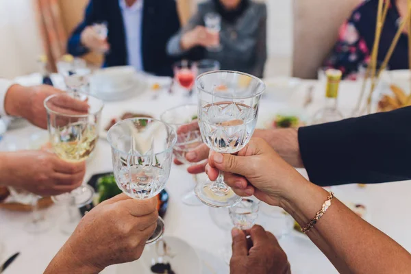 Close up shot of group of people clinking glasses with wine or champagne in front of bokeh background. older people hands