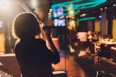 Genç kadın karaokede şarkı söylüyor ve mikrofonu yakın çekimde tutuyor. Parlak bir yıldız ve duman arka planda bir parti veya konserde Şarkıcı.