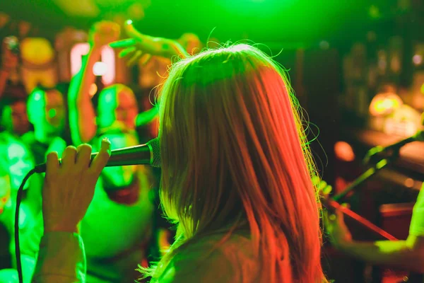 Młoda kobieta śpiewa w karaoke i trzyma mikrofon zbliżenie. Piosenkarka na imprezie lub koncert na tle świetlistej gwiazdy i dymu. — Zdjęcie stockowe