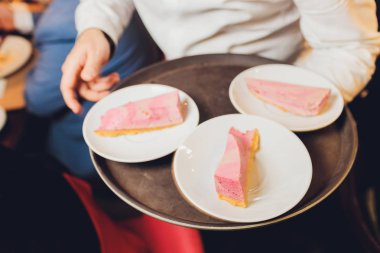bir plaka üzerinde beyaz çikolata ahududu cheesecake ve dilimlenmiş cheesecake bezle siyah bir taş tepsi ve bir beyaz ahşap masa, yukarıdan görünüm, yakın çekim dondurulmuş ahududu bölümünü.