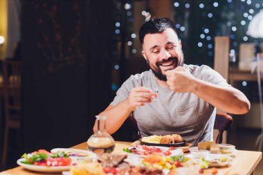 Adam büyük bir masada votka içiyor. Yanında yiyecek ve abur cubur var..