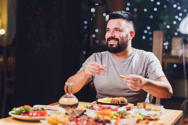 Adam büyük bir masada votka içiyor. Yanında yiyecek ve abur cubur var..