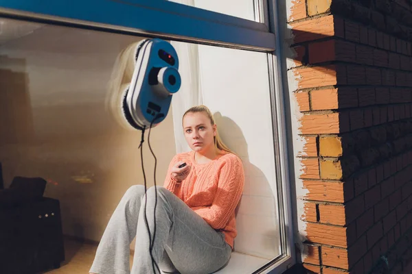 Ventana de limpieza robot aspiradora en edificio alto al aire libre. mujer joven controla el control remoto — Foto de Stock