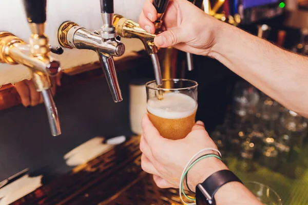 Close up of a male bartender dispensing draught beer in a pub holding a large glass tankard under a spigot attachment on a stainless steel keg.