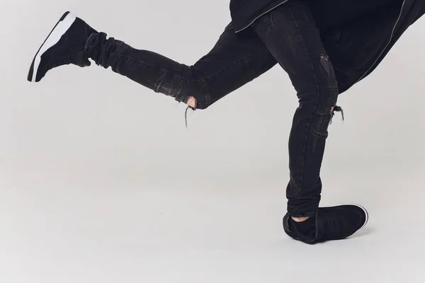 Close-up, Handsome young dancer dressed in black pants, a sweatshirt on a naked torso lifts one leg up while dancing street dance.