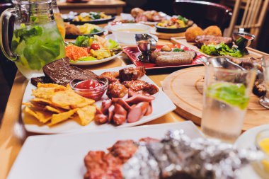 Yemek masası ile et ızgara, kızartma yeni patates, sebze, salata, soslar, aperatifler ve limonata, üstten görünüm.