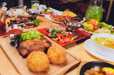 Yemek masası ile et ızgara, kızartma yeni patates, sebze, salata, soslar, aperatifler ve limonata, üstten görünüm.