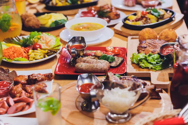 Вечеря на вечірці концепція їжі. Обідній стіл з ковбасою на грилі, обгортання тортильї, пивний напій та різні страви на дерев'яному столі, сільський стиль . — стокове фото