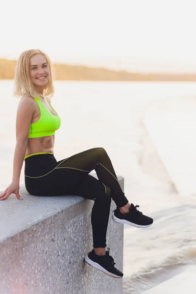 Egészséges nő, tengerparti sétányon edz. Fiatal vonzó nő sportruházatban nyújtózkodik edzés előtt a strandon napkeltekor. Melegíts be.. — Stock Fotó