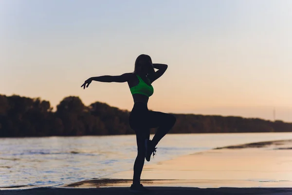 Silhueta de uma menina que dança em um campo em um fundo por do sol . — Fotografia de Stock