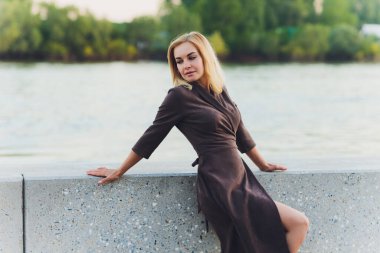 Açık havada, uzun düz saçlı, kısa siyah elbiseli, kahverengi deri çantalı, caddede yürüyen beyaz bir kadının portresi..