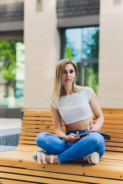 Mädchen schreibt in ein Notizbuch, sitzt auf einer Bank im Park. — Stockfoto