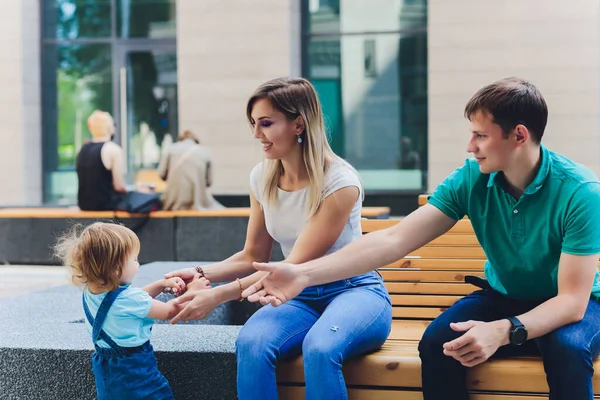 Familie portret moeder en vader zitten op de bank in het stadspark met baby meisje praten en glimlachen. Samen wandelen in het weekend. Moeder, vader, klein meisje dat samen tijd doorbrengt. Kinderopvang en ouderschap. — Stockfoto