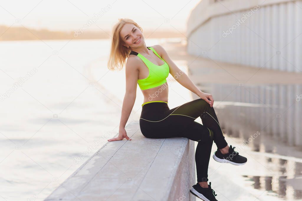 Healthy woman training on seaside promenade. Young attractive woman in sportswear does stretching before exercise on the beach at sunrise. Warm up.