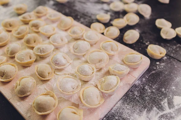 Surowe pierogi na czarnym tle, mąka, wałek, łyżka, płaskie układanie, poziomo. — Zdjęcie stockowe