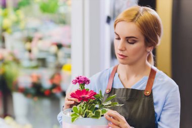 Çiçekçi olarak çalışan ve arka planda müşterisi olan bir kadın satış görevlisi. Yatay şekil, bel yukarı.