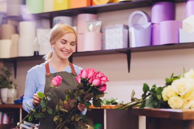 Çiçekçi olarak çalışan ve arka planda müşterisi olan bir kadın satış görevlisi. Yatay şekil, bel yukarı.