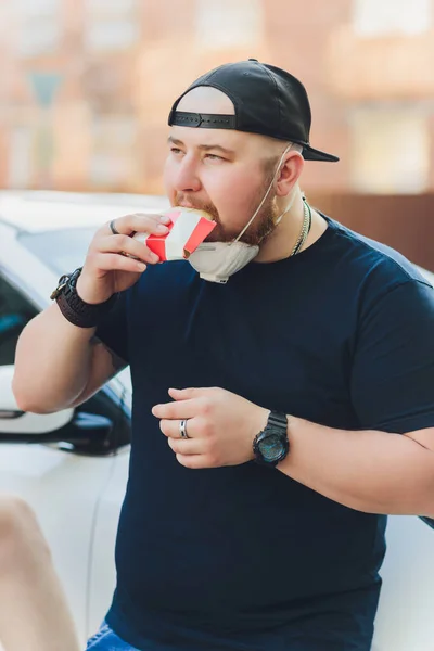 Молодой турист в медицинской маске ест уличную еду на пешеходной улице. Пряный фаст-фуд . — стоковое фото