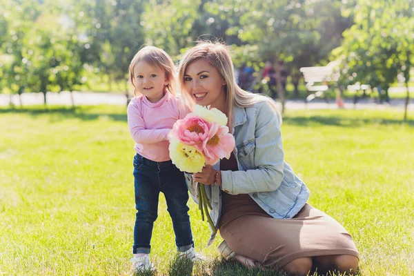 Gelukkige Moederdag Dochter feliciteert moeder en geeft haar bloemen boeket pioenrozen. Mam en meisje glimlachend en knuffelend. Familie vakantie en samenzijn. — Stockfoto