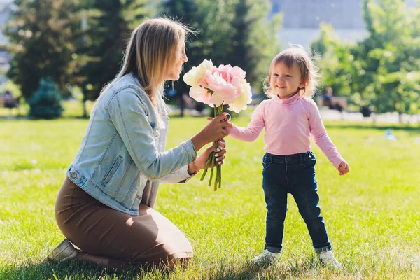 Gelukkige Moederdag Dochter feliciteert moeder en geeft haar bloemen boeket pioenrozen. Mam en meisje glimlachend en knuffelend. Familie vakantie en samenzijn. — Stockfoto