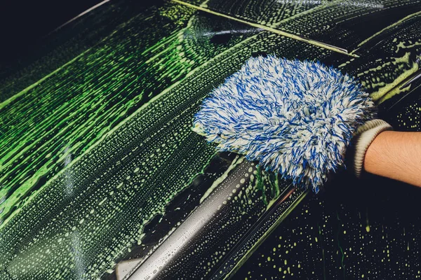 Myčka aut ručně. Mýdlové nálevky, bublinky a rukavice. Muž myje auto ručně. — Stock fotografie