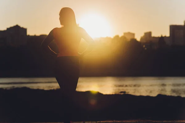 Happy successful sportswoman raising arms to the sky on golden back lighting sunset summer. Fitness athlete with arms up celebrating goals after sport exercising and working out outdoors. Copy space.