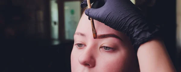 Maquilhagem. Mãos de esteticista fazendo tatuagem de sobrancelha no rosto da mulher. Closeup de especialista fazendo tatuagem de sobrancelha para fêmea. Cosmetologia Tratamento . — Fotografia de Stock