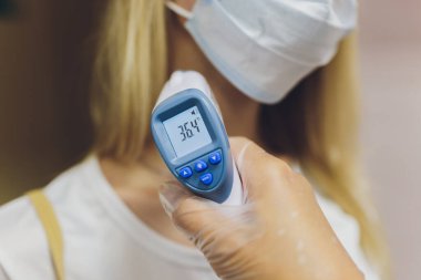 Doktor koruyucu bir eldiven verdi, bir kızılötesi termometre tutuyor ve hastanın sıcaklığını ölçüyor. Koronovirüs hastası bir salgın sırasında yüksek ateşin uzaktan ölçümü..