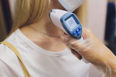 Doktor koruyucu bir eldiven verdi, bir kızılötesi termometre tutuyor ve hastanın sıcaklığını ölçüyor. Koronovirüs hastası bir salgın sırasında yüksek ateşin uzaktan ölçümü..