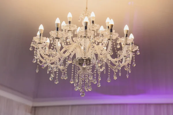 Small lamp as stars at big chandelier with many crystals. — Stock Photo, Image