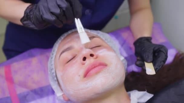 Ovanifrån av vacker ung kvinna att få ansiktshud behandling. Kosmetiker genomför förfarandet med grädde. — Stockvideo