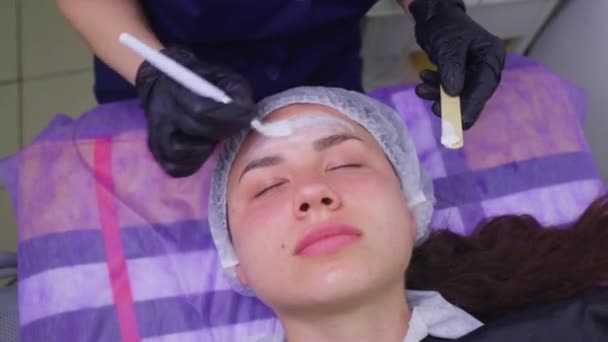 Top view of beautiful young woman getting face skin treatment. Cosmetician is undertaking the procedure applying cream. — Stock Video