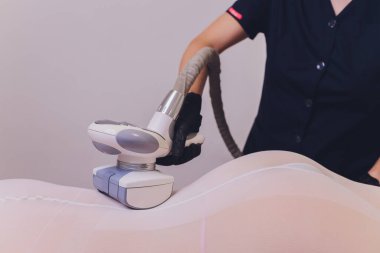 Beyaz takım elbiseli kadın vücudu spa aletleriyle anti-selülit masajı yaptırıyor..