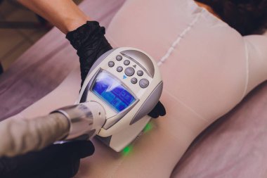 Beyaz takım elbiseli kadın vücudu spa aletleriyle anti-selülit masajı yaptırıyor..