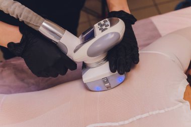 Beyaz takım elbiseli kadın vücudu spa aletleriyle anti-selülit masajı yaptırıyor..