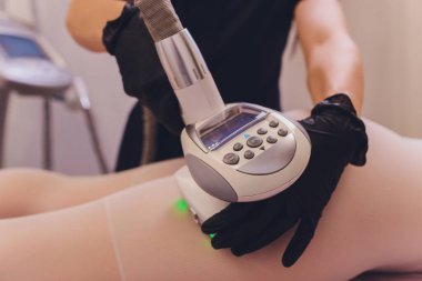 Beyaz takım elbiseli kadın vücudu spa aletleriyle anti-selülit masajı yaptırıyor..