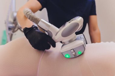 Beyaz takım elbiseli kadın vücudu spa aletleriyle anti-selülit masajı yaptırıyor..