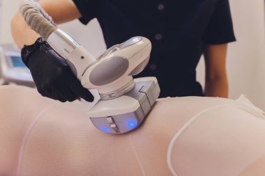 Beyaz takım elbiseli kadın vücudu spa aletleriyle anti-selülit masajı yaptırıyor..
