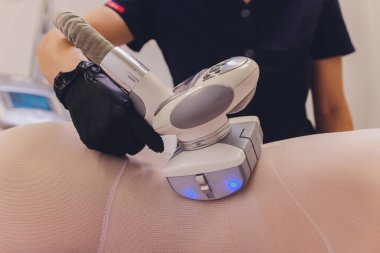Beyaz takım elbiseli kadın vücudu spa aletleriyle anti-selülit masajı yaptırıyor..