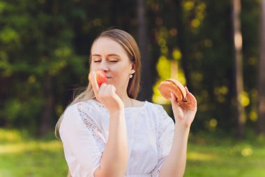 Gülümseyen kadın dışarıda öğle yemeği molası veriyor, çimlerin üzerinde oturuyor ve yemek yiyor..