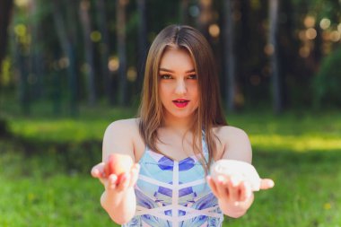 Gülümseyen kadın dışarıda öğle yemeği molası veriyor, çimlerin üzerinde oturuyor ve yemek yiyor..