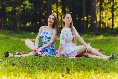 Gülümseyen kadın dışarıda öğle yemeği molası veriyor, çimlerin üzerinde oturuyor ve yemek yiyor..